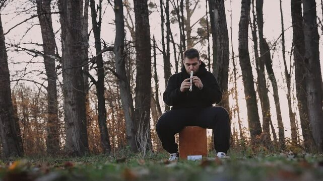 A young man in a black sweatshirt plays on panpipe enchanting melodies in the autumn park