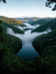 Obraz premium Aerial view of a lake surrounded by lush green mountains and fog.