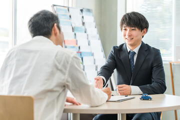 男性客と商談・接客・打ち合わせする若いアジア人ビジネスマン（自動車・保険）
