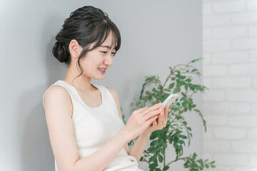 家で笑顔でスマホを使うアジア人女性
