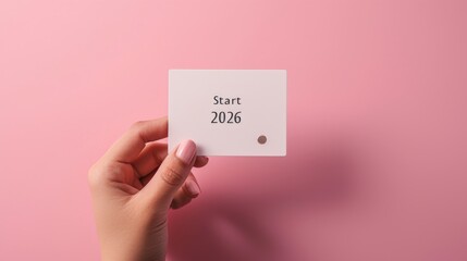 A simple card with Start 2026 text held by a hand against a pink background. This clean and modern image highlights clarity and optimism. AI generated.