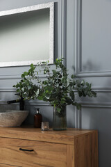 Eucalyptus branches and candle near vessel sink on bathroom vanity. Interior design