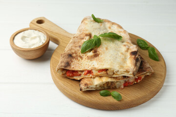 Halves of tasty calzone with meat, cheese, tomato, basil and sauce on white wooden table, closeup