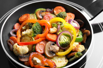 Frying pan with mix of vegetables and mushrooms on cooktop, closeup
