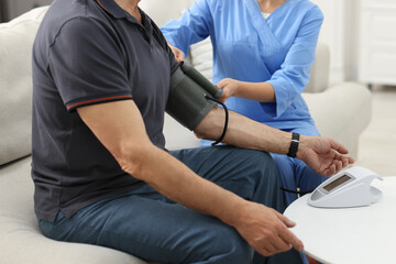 Nurse measuring senior man's blood pressure at home, closeup