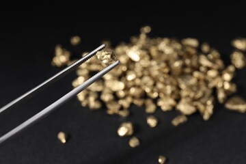 Tweezers with gold nugget against blurred background, closeup. Space for text