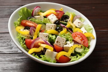 Delicious fresh Greek salad in bowl on wooden table, closeup