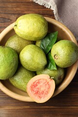 Fresh cut and whole guava fruits in bowl on wooden table, top view