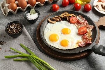 Tasty fried eggs with bacon and mushrooms served on grey table