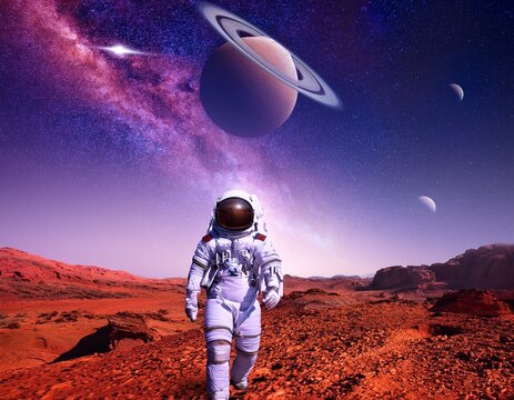 Un astronaute en combinaison spatiale marchant sur une exoplan&egrave;te rouge&acirc;tre, sous un ciel violet rempli de plan&egrave;tes et d&rsquo;&eacute;toiles scintillantes