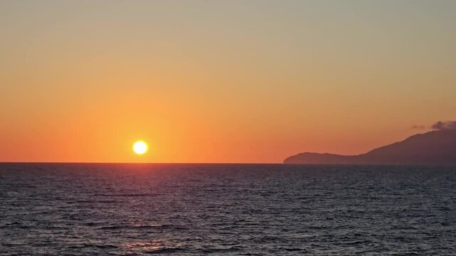 Golden sun in an orange and amber colored sky just above tranquil ocean horizon off the tip of an Ionian island as viewed from shipboard.
