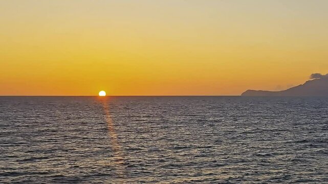 Golden setting sun slowly sinks out of sight into the tranquil waters of the Ionian Sea