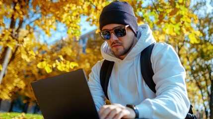 Fototapeta premium Young Man Working on Laptop Outdoors in Bright Autumn Leaves