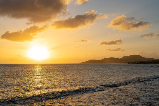 Golden sunset over the ocean with the sun casting a warm glow on the water and silhouetted mountains in the distance. Vieques, Puerto Rico.