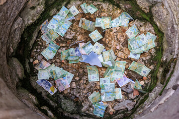 Fototapeta premium Scattered currency notes in a water-filled stone well