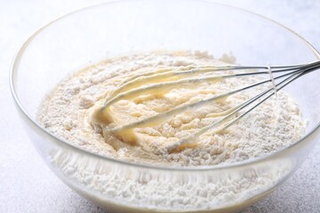Whisk and bowl of dough on table, closeup