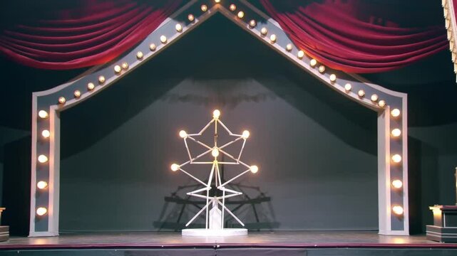 This is a stage setup featuring a rectangular proscenium arch with rounded corners, illuminated by evenly spaced lightbulbs along its inner edge.