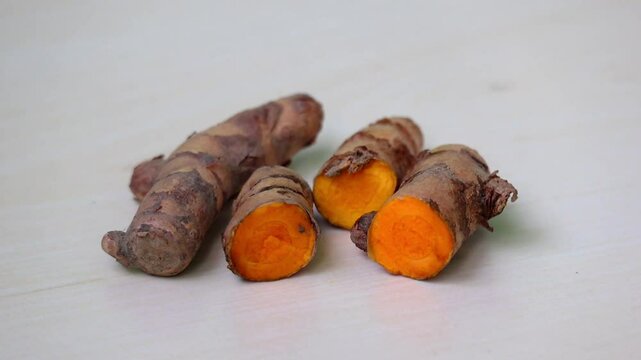 Close-up of fresh, raw turmeric, whole and sliced in half, on a wooden surface. 