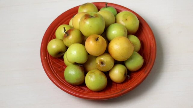 Fresh, ripe plum fruits are arranged on a clay plate resting on a wooden surface. These fruits, known as Boroi or Kul in Bangladesh, are also called Indian jujube, Chinese date, or Chinee apple.