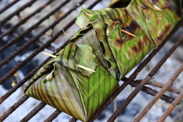 Food wrapped in banana leaves, grilled on a stove with low heat.