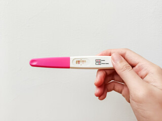 A close-up of a hand holding a pregnancy test with a pink handle against a plain white background. The test features two result windows with labels in Indonesian: 'HAMIL' (pregnant) and 'TIDAK HAMIL' 