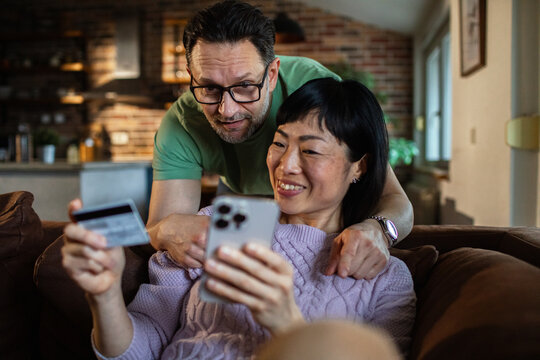 Happy couple shopping online with smartphone and credit card on couch at home