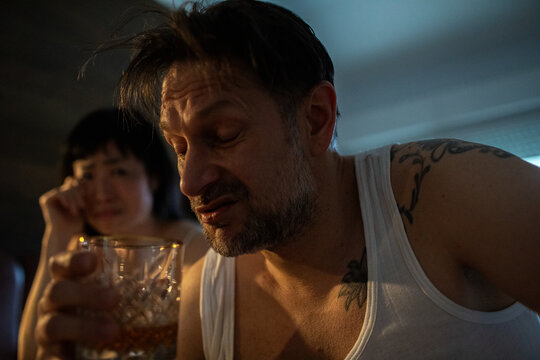 Man drinking alcohol while woman cries in background