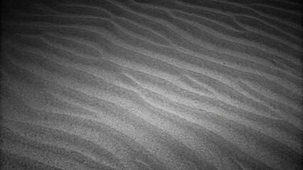 Fototapeta premium Wavy beach sand texture. Black and white with vignette. Grainy grunge abstract background. Black Sand dune. Black Sand beach macro photography. The wave pattern of oceanic sand on the beach black.