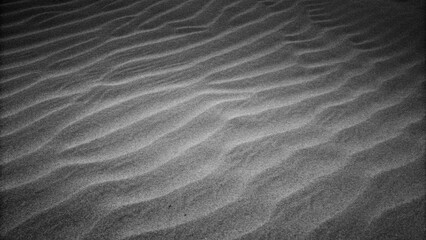 Obraz premium Wavy beach sand texture. Black and white with vignette. Grainy grunge abstract background. Black Sand dune. Black Sand beach macro photography. The wave pattern of oceanic sand on the beach black.