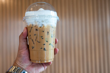 Iced coffee latte with milk cream topping on man hand. Summer refreshment drink concept