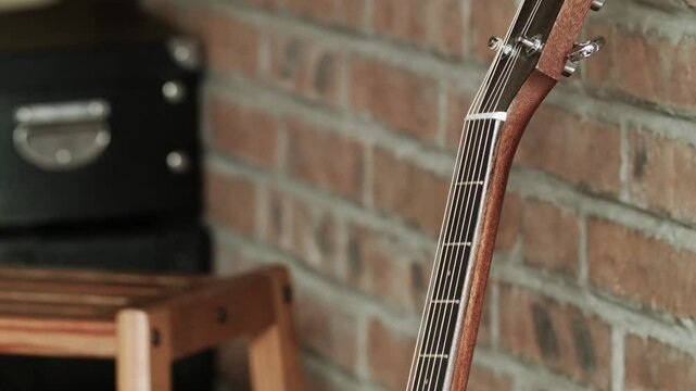 A hand reaches out and places a small note with a smiley face on it on the strings of a guitar leaning against a brick wall. The scene suggests a moment of personal affection or playful action.