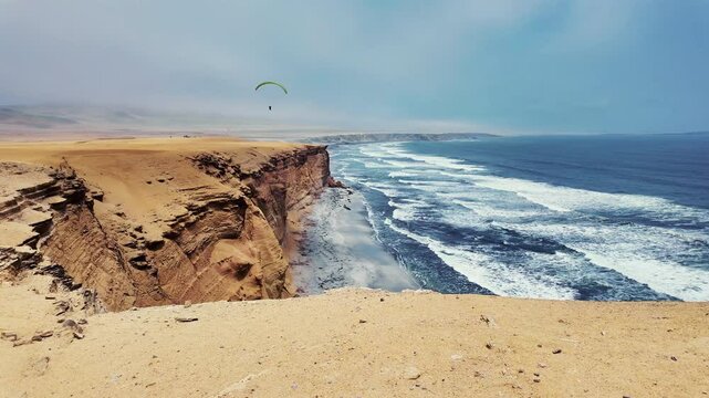 Paracas National Reserve on a cloudy, windy day with a paraglider in the background performing aerial maneuvers.