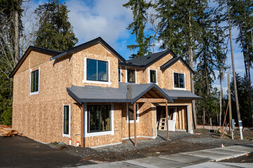 New home construction site, house framed with roof covered with protective membrane, windows installed, job site on a sunny winter day
