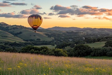 Obraz premium Hot air balloon ascends over rolling hills at sunset, wildflowers in foreground. Perfect for travel, adventure, and peaceful nature imagery.