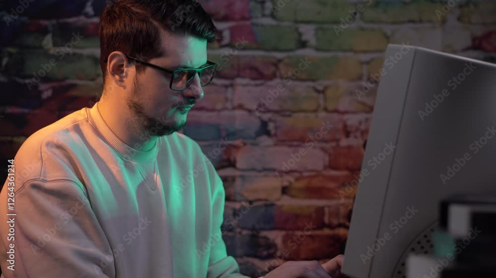 Poster young man with glasses working on desktop computer from 1990's, typing on keyboard and looking at cr