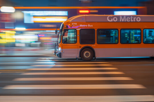 LOS ANGELES, CA - February 12, 2025: Orange Metro bus rushing through city traffic, crossing illuminated street intersection at night on Santa Monica Blvd in West Hollywood, California.