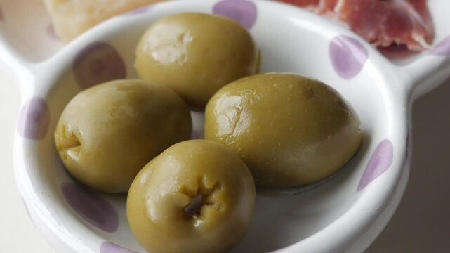 Olives in a bowl, part of a traditional tapas spread with cheese, jamon, and colines