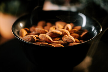 Almonds arranged in a dark plate radiating natural textures and hues on a black background