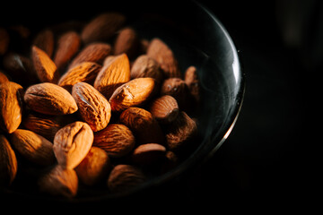 Natural almonds on a plate isolated against a dark black background creating a striking visual contrast