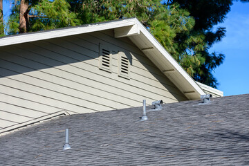 Sloped asphalt shingle roof with multiple metal vents, beige siding, and attic air vents