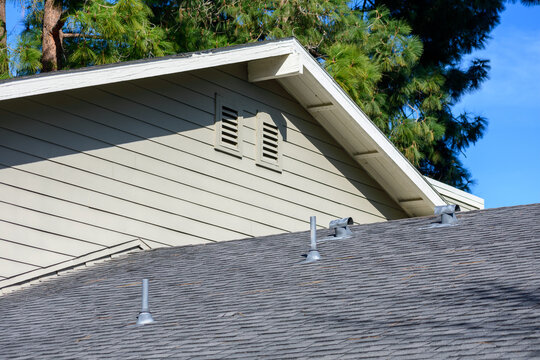Sloped asphalt shingle roof with multiple metal vents, beige siding, and attic air vents