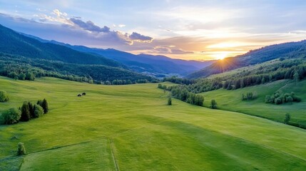 Fototapeta premium Lush Green Meadow Valley Surrounded by Forested Mountains at Golden Sunset Sunlight
