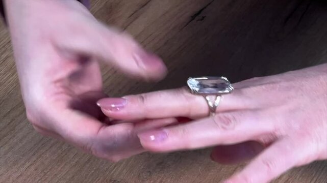 A woman puts a ring with a large transparent stone on her finger. She examines it and shows it off. Close-up.