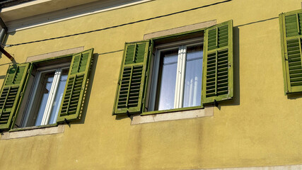 Green shuttered windows on a mustard yellow wall, European architecture, vibrant summer atmosphere