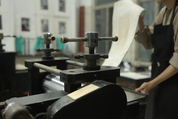 A Close up of a printmaker carefully lifts a print from an etching press in a workshop. The Art of Printmaking, Printing with an Etching Press concept