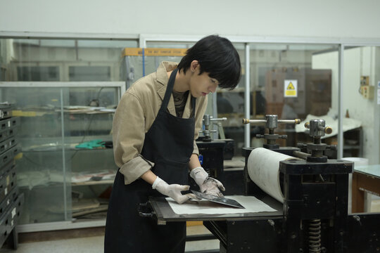 A young printmaker places an inked etching plate onto the etching press machine, ensuring precise alignment for a successful intaglio print in a workshop studio