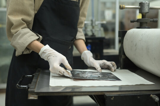 A Close-up of a young artist carefully aligning an inked etching plate onto damp paper before running it through the press, Art of Printmaking concept