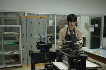 A young artist in a printmaking workshop stands beside an etching press, preparing for the next...