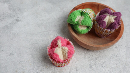 Colorful Bolu Kukus (Sponge Cake), made from flour, tapioca flour, egg and sugar. Served on wooden plate isolated on grey background. Indonesian traditional snack