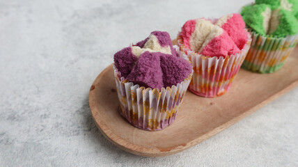 Colorful Bolu Kukus (Sponge Cake), made from flour, tapioca flour, egg and sugar. Served on wooden plate isolated on grey background. Indonesian traditional snack